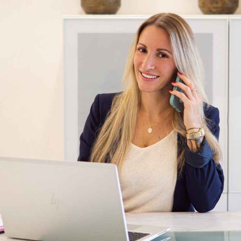 Junge Frau am Schreibtisch, telefonierend mit einem Laptop vor ihr.