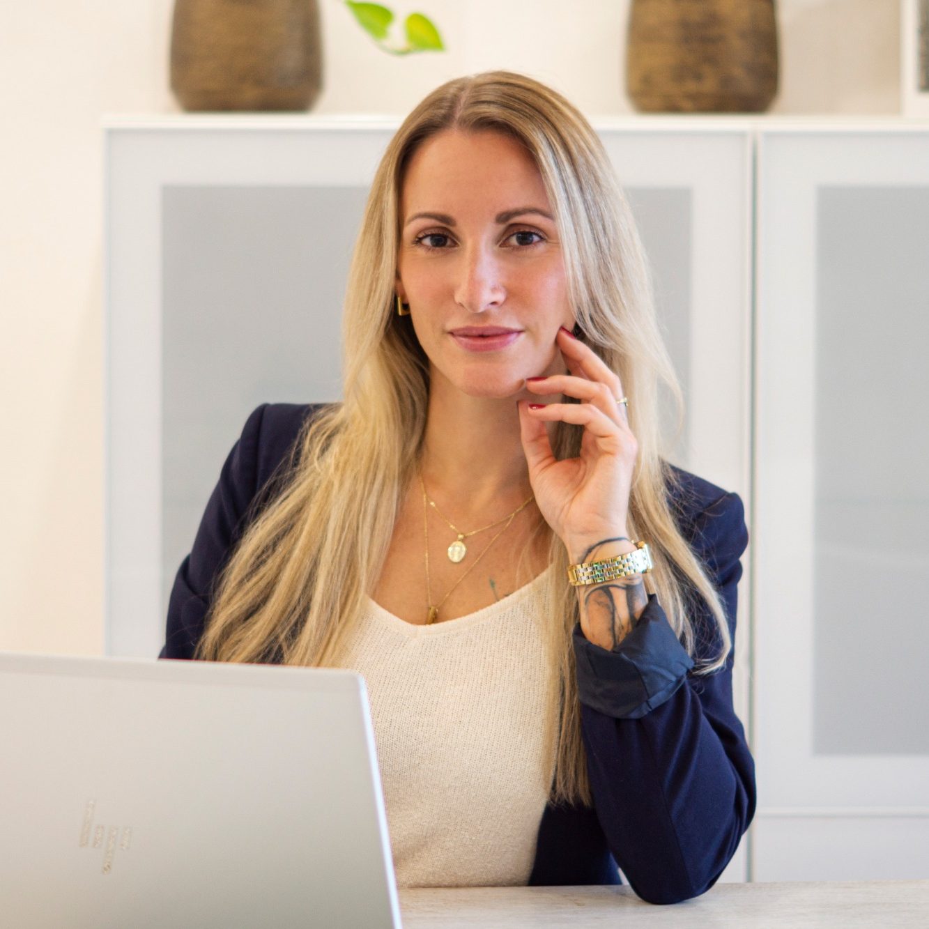 Frau mit langen blonden Haaren, sitzt am Schreibtisch und schaut nachdenklich.