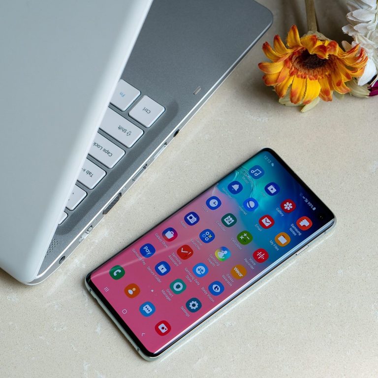 Smartphone mit bunten App-Symbolen neben einem Laptop und einer Blume.