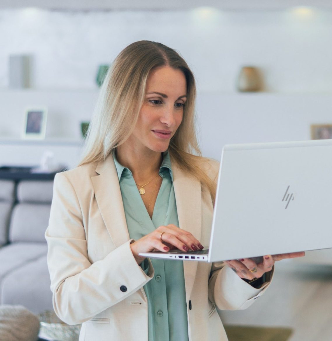 Frau mit blonden Haaren arbeitet an einem Laptop in einem hellen, modernen Raum.